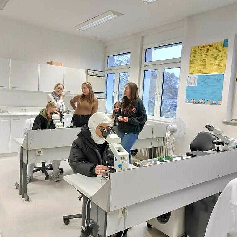 Schüler*innen arbeiten konzentriert in einem Labor mit Mikroskopen, während sie unter Anleitung praktische Experimente durchführen.