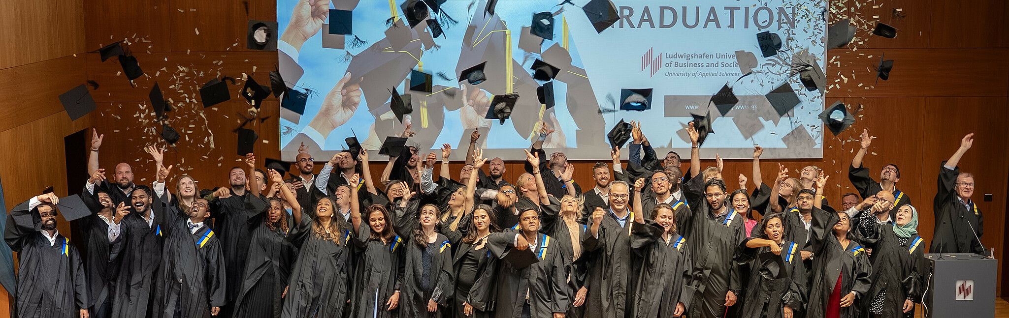 @GSRN Absolvent*innen werfen auf der Bühne ihre Absolventenhüte und Konfetti in die Luft