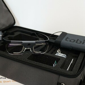 Zusehen ist die Equipment Tasche der Eyetrackingbrill. Der geöffnete Deckel zeigt das Innenleben mit diversen Zusatzteilen. Oben auf liegt die Brill und der Akku.