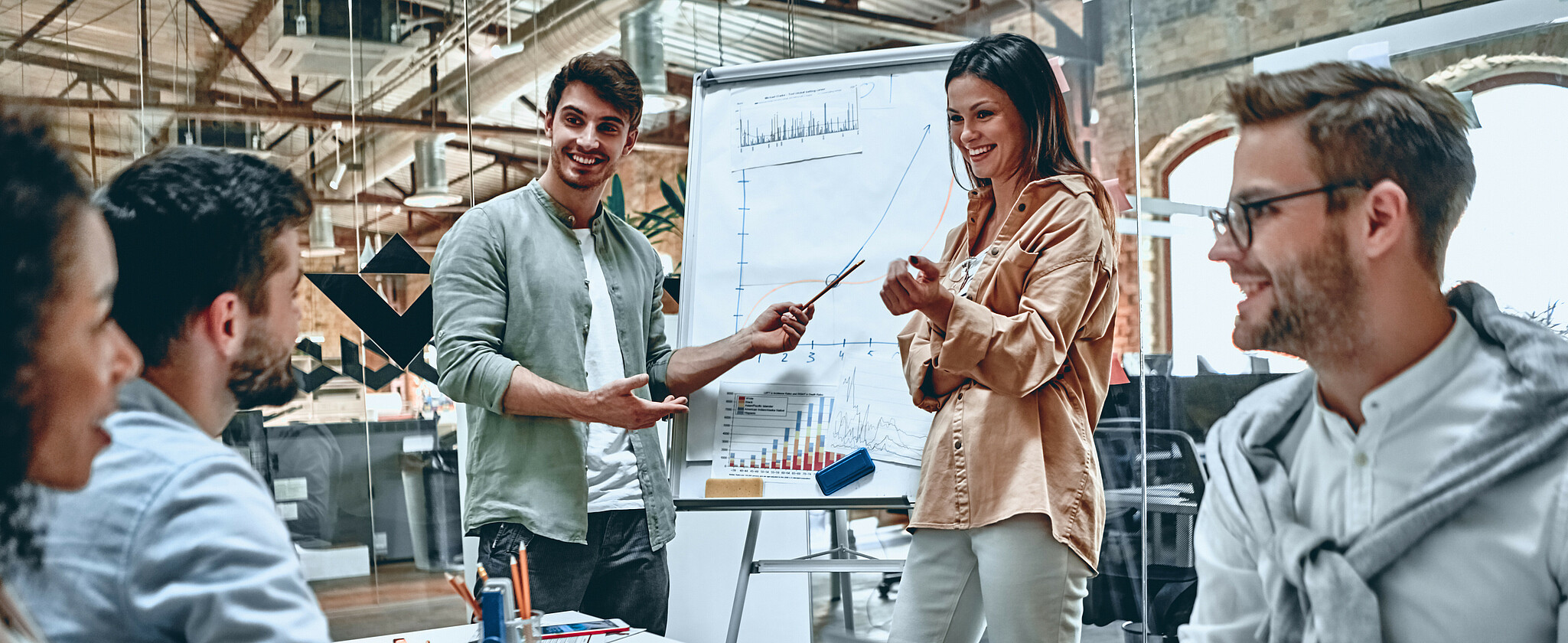 Gruppe fröhlicher junger Leute mit Flipchart und Laptops