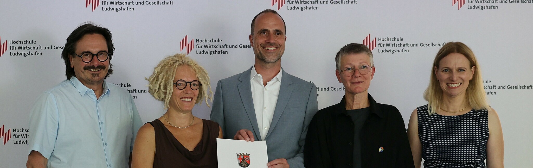 Wissenschaftsminister Clemens Hoch (M.) übergibt den Förderbescheid für das Projekt „PRO.SOZIAL“ an der Hochschule für Wirtschaft und Gesellschaft Ludwigshafen an die Antragstellerinnen Prof. Dr. Marion Ott (2.v.l.) und Prof. Dr. Karen Wagels (2.v.r.) im Beisein von Dekan Prof. Dr. Peter Rahn und Vizepräsidentin Prof. Dr. Edith Rüger-Muck.