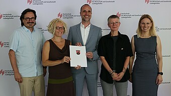 Wissenschaftsminister Clemens Hoch (M.) übergibt den Förderbescheid für das Projekt „PRO.SOZIAL“ an der Hochschule für Wirtschaft und Gesellschaft Ludwigshafen an die Antragstellerinnen Prof. Dr. Marion Ott (2.v.l.) und Prof. Dr. Karen Wagels (2.v.r.) im Beisein von Dekan Prof. Dr. Peter Rahn und Vizepräsidentin Prof. Dr. Edith Rüger-Muck.